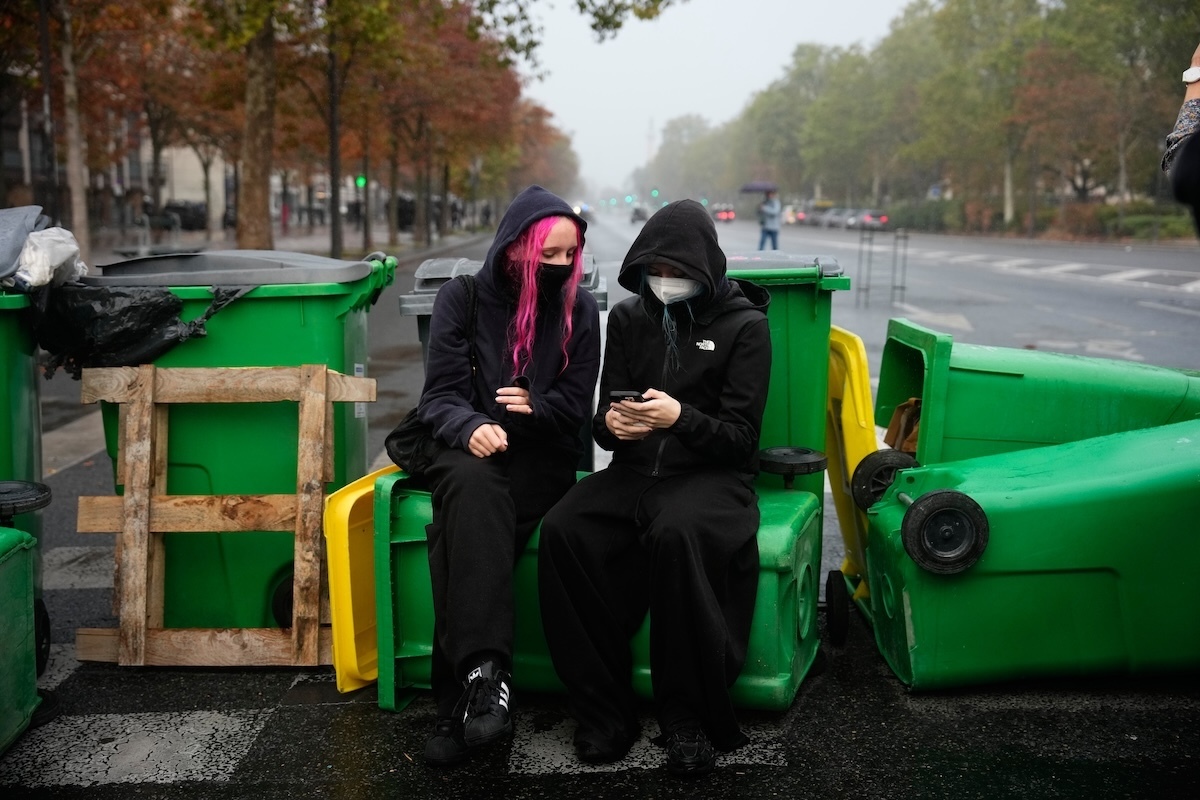 Due studentesse guardano il cellulare sedute su cassonetti della spazzatura, che bloccano la strada nei pressi del liceo Hélène-Boucher (AP Photo/Teresa Suarez)