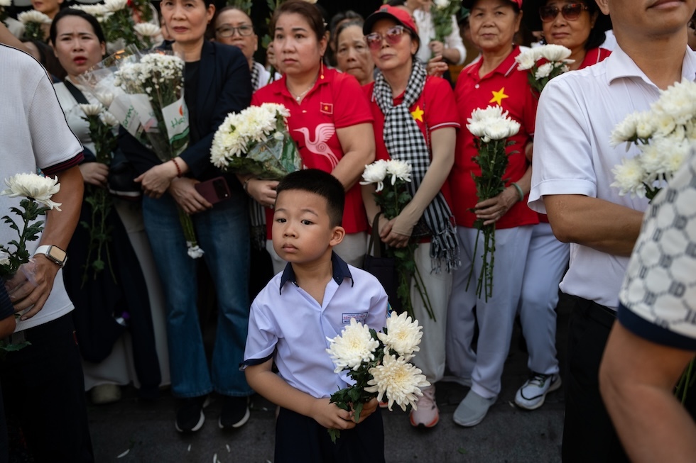 Un bambino e un gruppo di persone, con mazzi di crisantemi bianchi in mano, assistono a una cerimonia commemorativa al parco Le Thi Rieng, dove sono stati ritrovati i resti di 731 persone, ritenute morte durante l’offensiva del Tet del 1968, una delle più grandi operazioni della guerra del Vietnam (AP Photo/Thanh Hue)