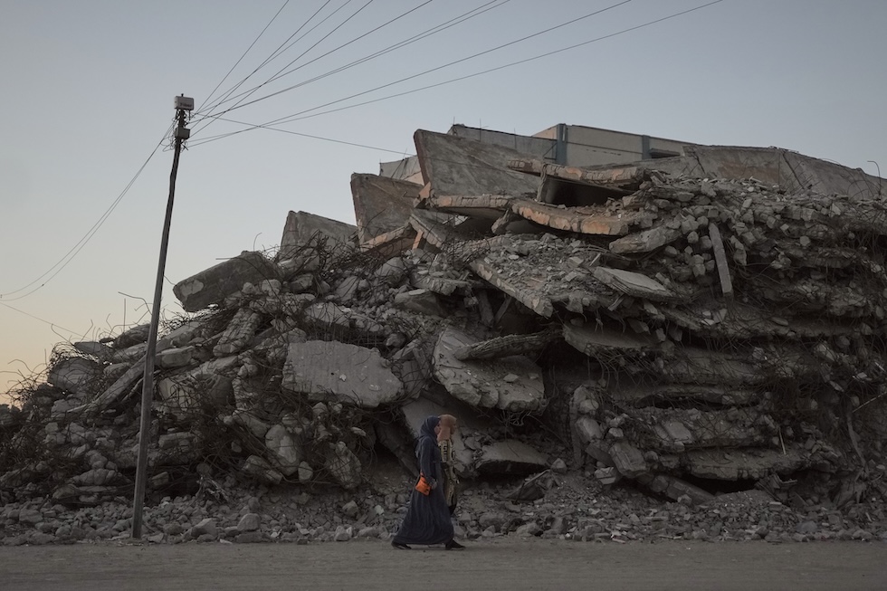 Due donne camminano in strada, passando accanto alle macerie di edifici distrutti (AP Photo/Jehad Alshrafi)