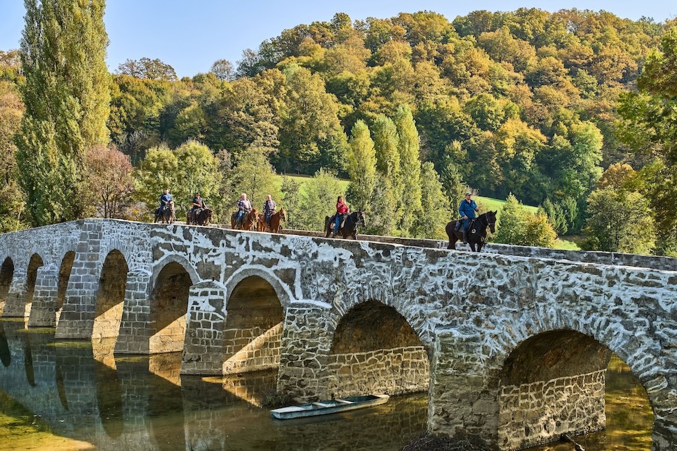 Persone a cavallo su un ponte sul fiume Dobra (AP Photo/Michael Probst)