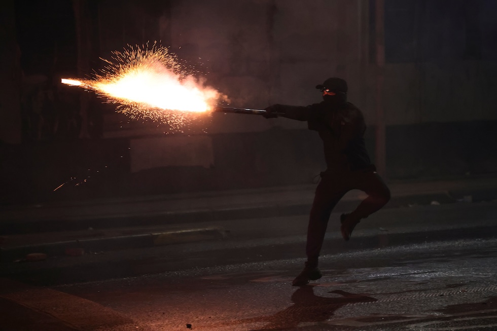 Un manifestante punta un fuoco d'artificio verso la polizia durante le proteste contro il governo, ieri 18 ottobre (AP Photo/Hameraldi Agolli)