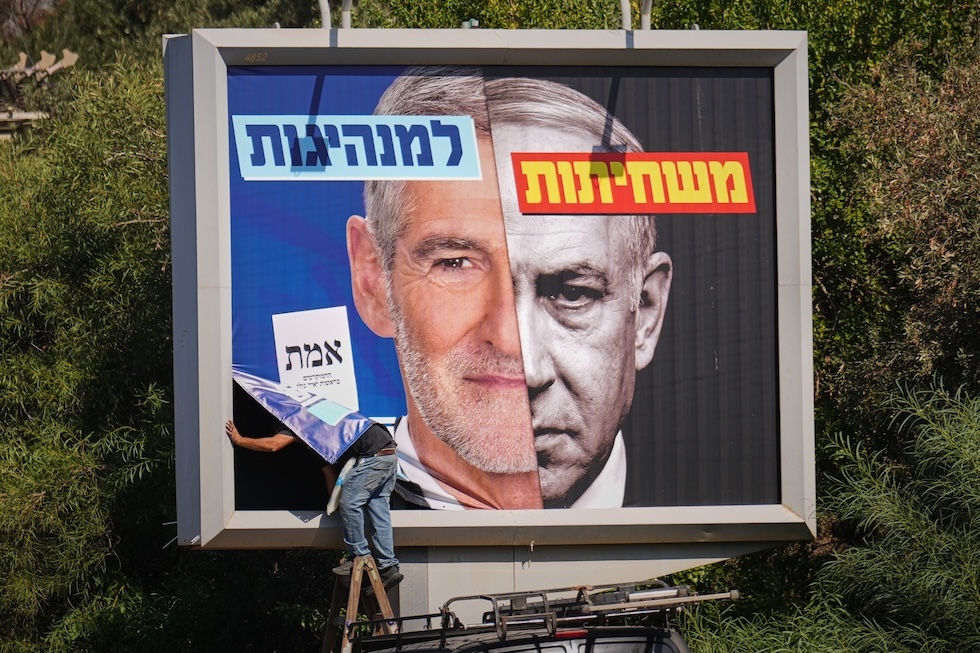 Un operaio affigge un manifesto della campagna elettorale con una foto del volto del leader dei Democratici, Yair Golan (a sinistra), accanto a quella del primo ministro israeliano Benjamin Netanyahu  (AP Photo/Ariel Schalit)
