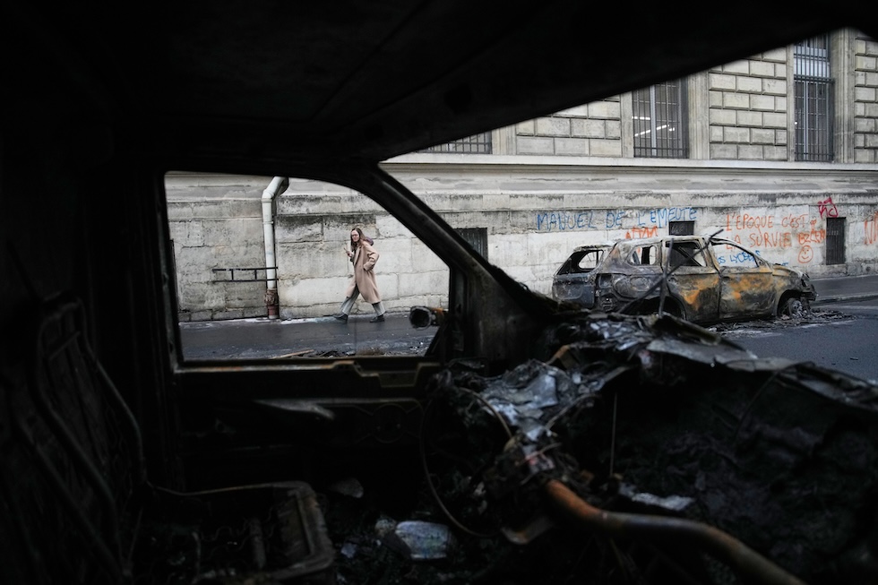 Una donna passa accanto ad alcune auto bruciate, dopo la prima notte di coprifuoco dall’inizio delle proteste  (AP Photo/Christophe Ena)
