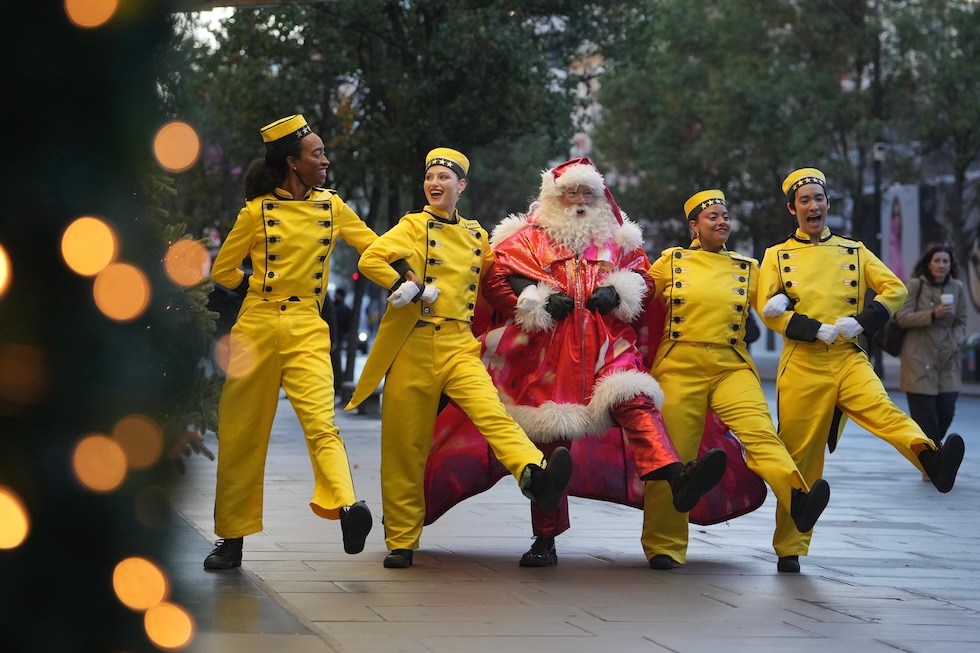 Una persona vestita da Babbo Natale e alcune donne vestite da facchini ballano davanti alle vetrine natalizie dei grandi magazzini Selfridges (AP Photo/Kin Cheung)
