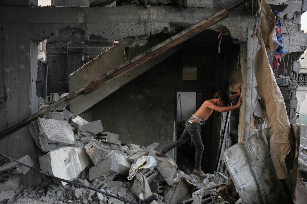 Un ragazzino palestinese tra le macerie di una casa distrutta nella notte da un attacco israeliano (AP Photo/Abdel Kareem Hana)