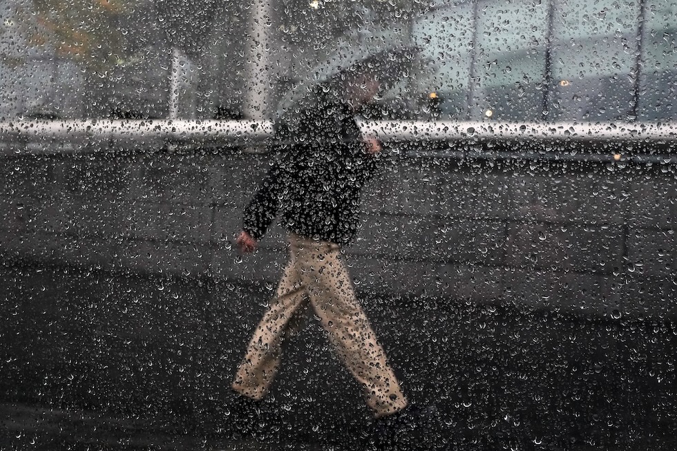 Una persona con un ombrello cammina sotto la pioggia, vista attraverso un vetro coperto di gocce d’acqua (AP Photo/Kirsty Wigglesworth)