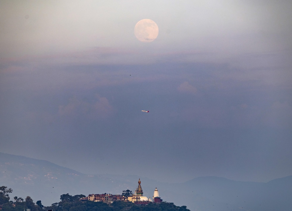 La luna piena sorge dietro il Tempio di Swayambhu, famoso luogo di culto buddista, mentre un aereo decolla. (ANSA/EPA/NARENDRA SHRESTHA)