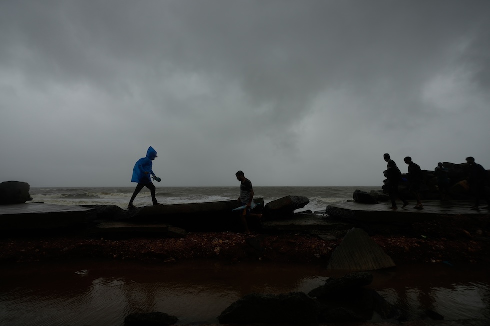 Persone camminano vicino alla costa su una strada danneggiata dal ciclone Arnab (AP Photo/Mahesh Kumar A.)
