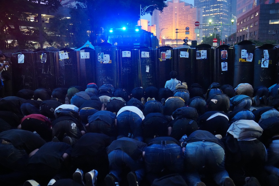 Studenti recitano la preghiera serale durante una protesta, mentre la polizia in tenuta antisommossa è schierata davanti a loro (AP Photo/Tatan Syuflana)