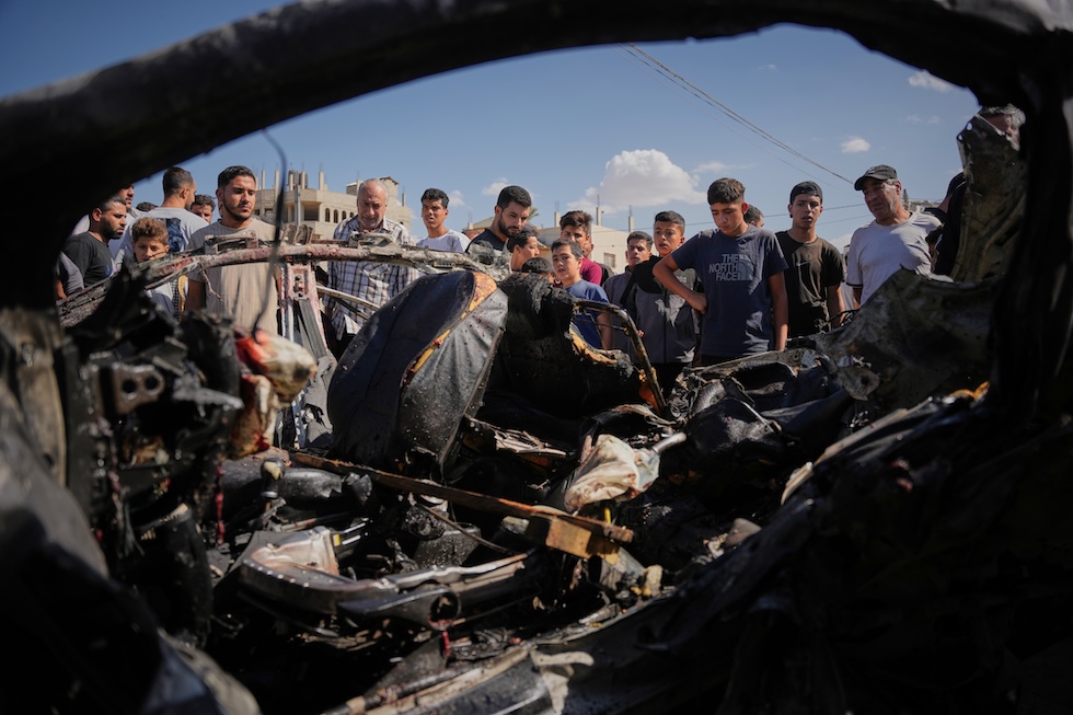 Palestinesi ispezionano i resti di un veicolo distrutto da un attacco aereo israeliano (AP Photo/Abdel Kareem Hana)