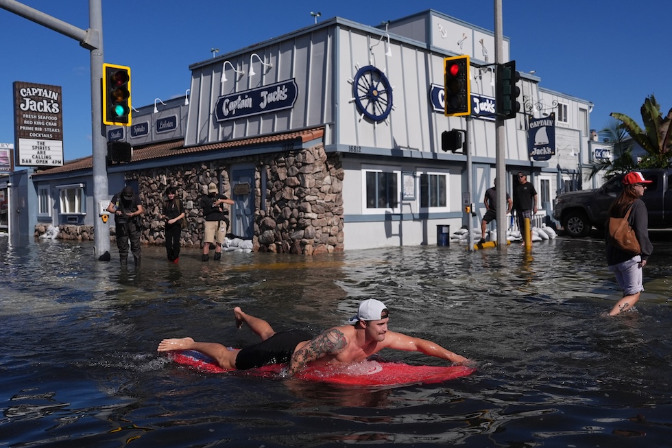 Un uomo si muove su una tavola da surf nelle strade allagate dall'alta marea (AP Photo/Jae C. Hong)