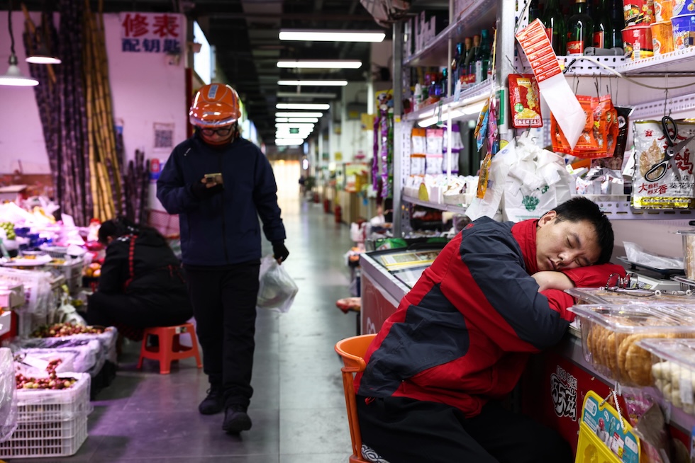 Un uomo dorme in un mercato della città, mentre un altro gli passa accanto (EPA/WU HAO via Annsa)