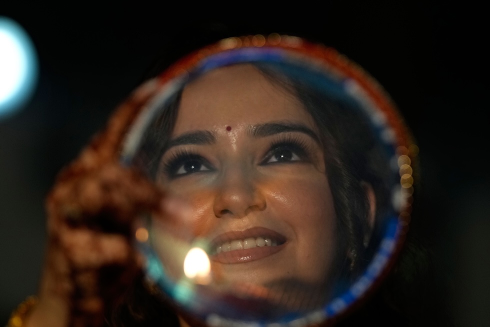 Una donna indù guarda la Luna attraverso un setaccio, un rituale della festa di Karwa Chauth che precede la fine del digiuno osservato per augurare lunga vita al marito (AP Photo/Channi Anand)
