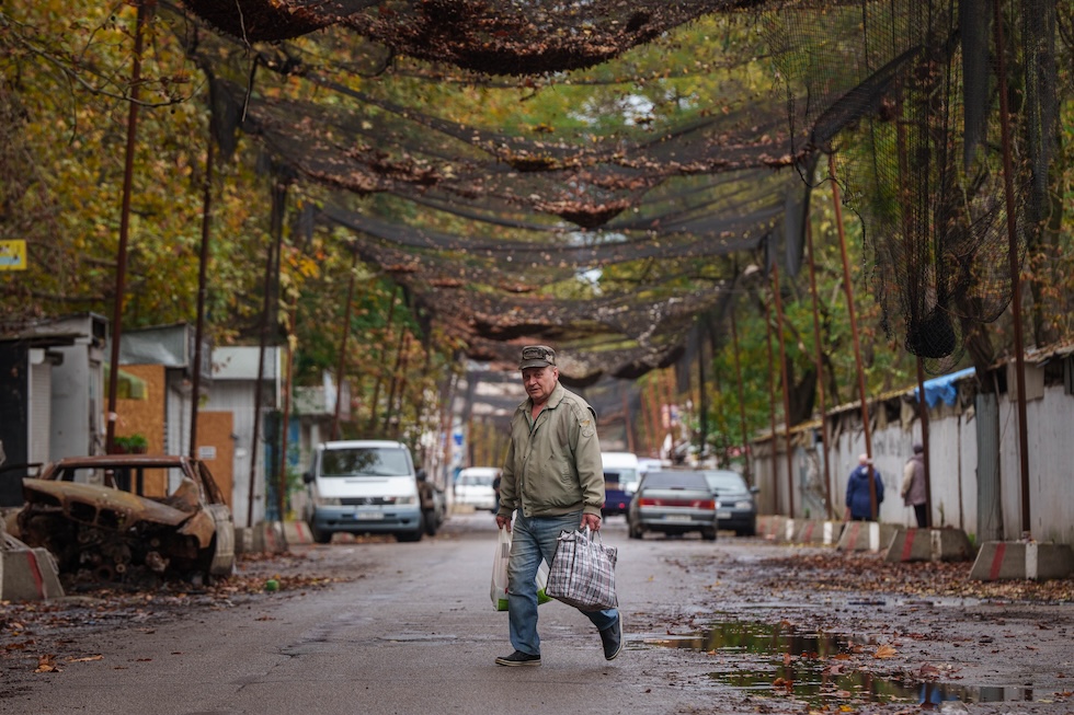 Un uomo attraversa una strada sotto le reti antidrone stese sopra la carreggiata (AP Photo/Evgeniy Maloletka)