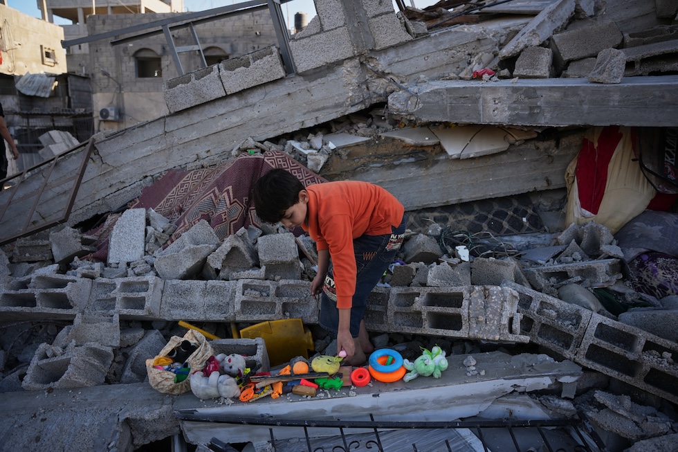 Un bambino cerca i suoi giocattoli tra le macerie della sua casa, distrutta durante la notte da un attacco aereo israeliano (AP Photo/Abdel Kareem Hana)
